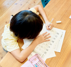 子供が教室の机で漢字を書く練習をしているところ。