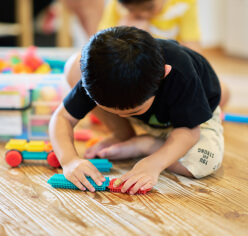 子供が教室で座りながらブロックのおもちゃで遊んでいるところ。