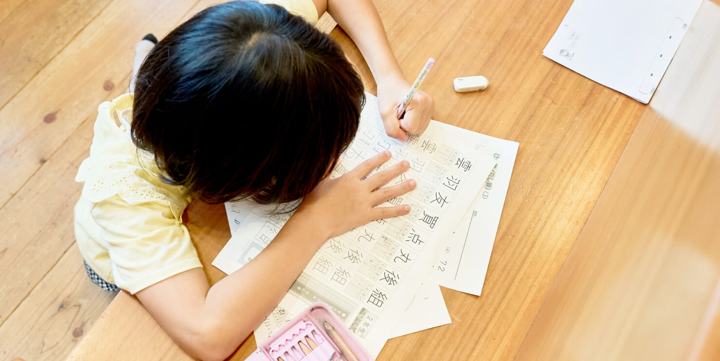 子供が教室の机で漢字を書く練習をしているところ。