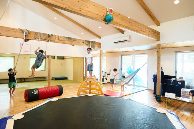 室内には大きなトランポリンやハンモック、奥に天井から吊るされたロープで遊ぶ子供達がいる。